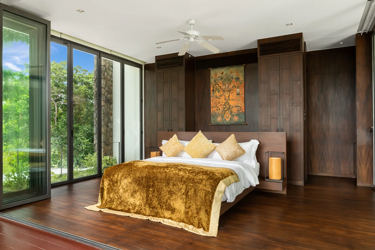 A bedroom with Thai artwork above the bed and a saffron velvet throw