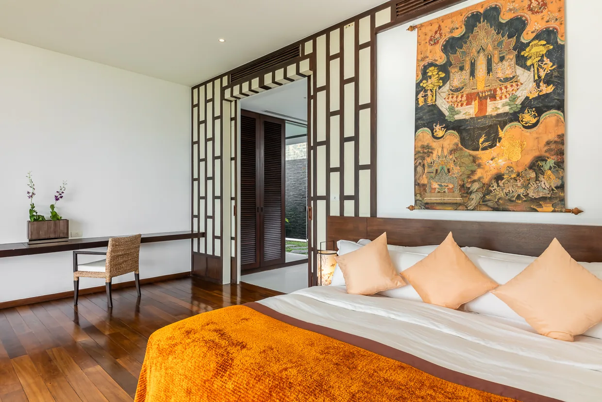 A bedroom with a Thai mural and a saffron bed cover
