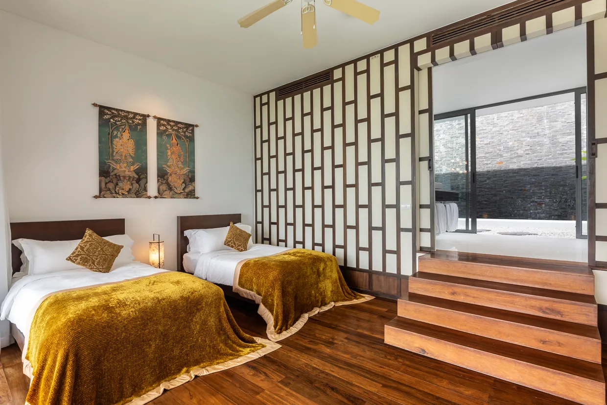 A twin bedroom with saffron throws behind a timber screen