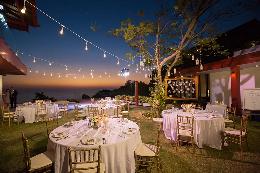 A wedding reception on the lawn under festoon lights at dusk